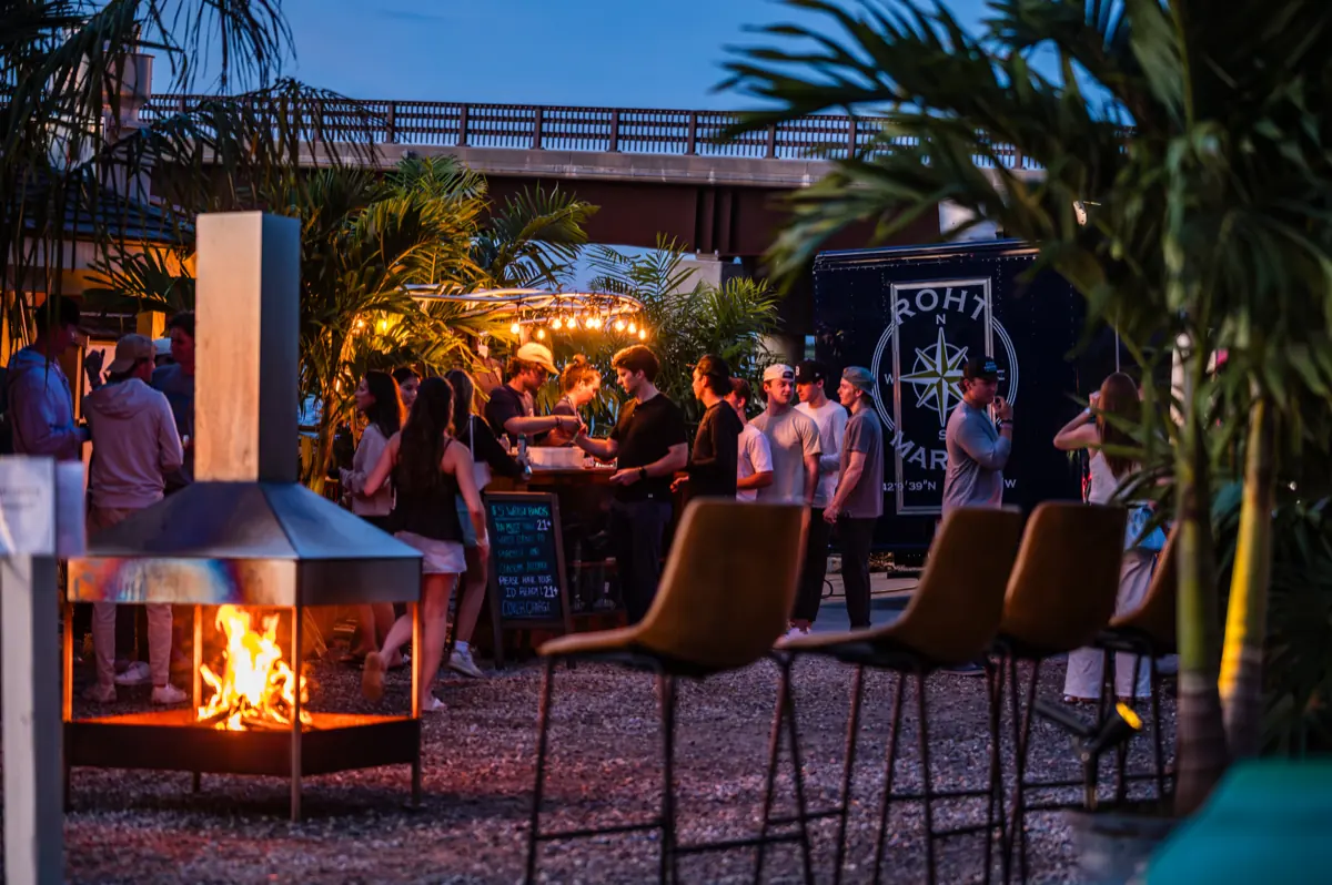 Guests gathered around a burning fire pit beside the ROHT Marine trailer bar at dusk