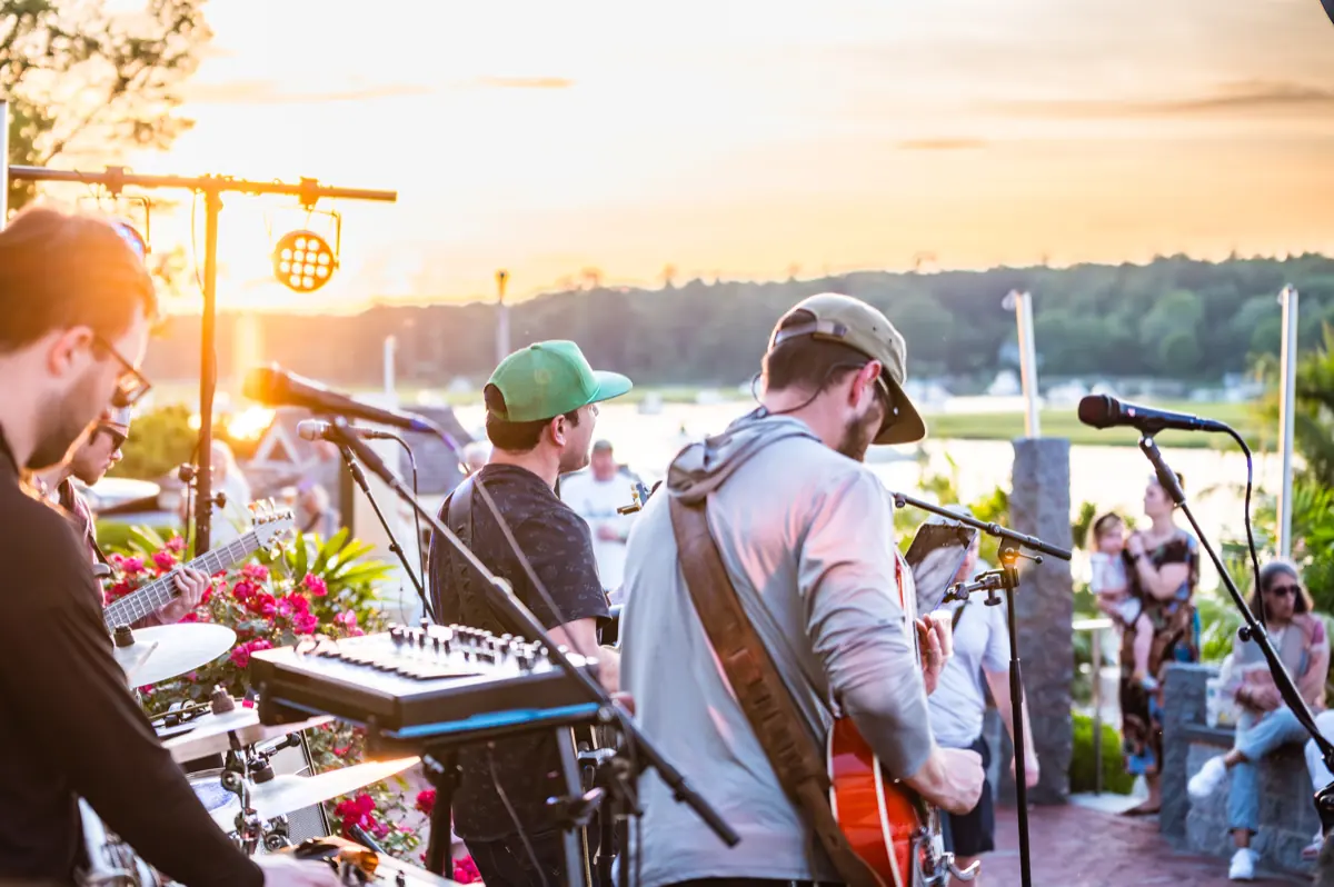 A band playing to a crowd on the waterfront as the sun sets behind the harbor