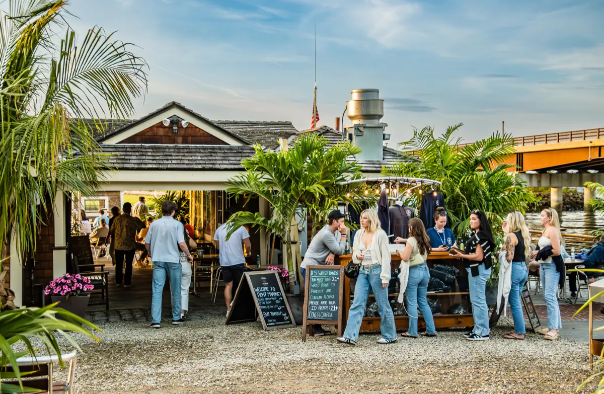 Guests crowded at the outdoor bar beneath chalkboard menus in golden light